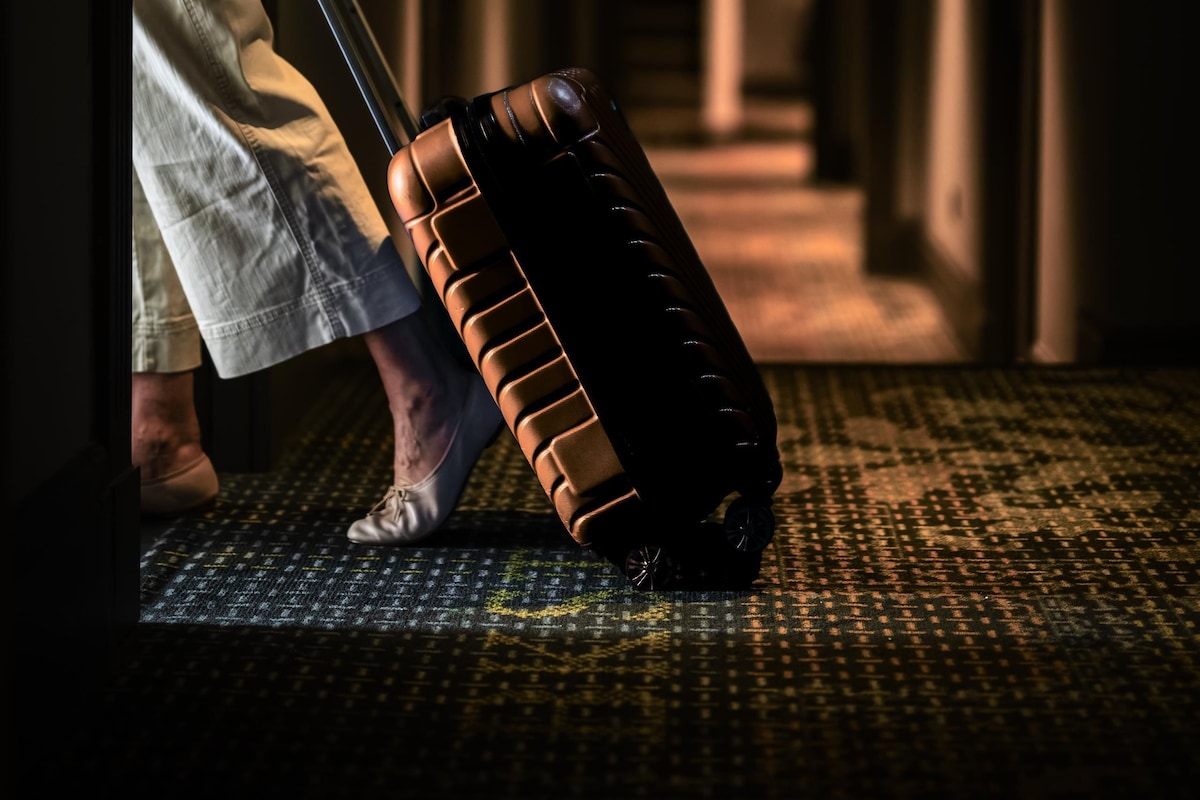 A person carrying a suitcase in a dimly lit hallway with patterned flooring.