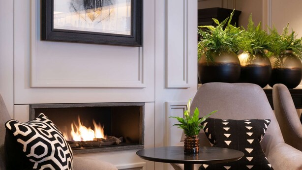 A modern living room with a fireplace, two armchairs, a round table, and a framed artwork above the fireplace. - Holmes Hotel London (London)