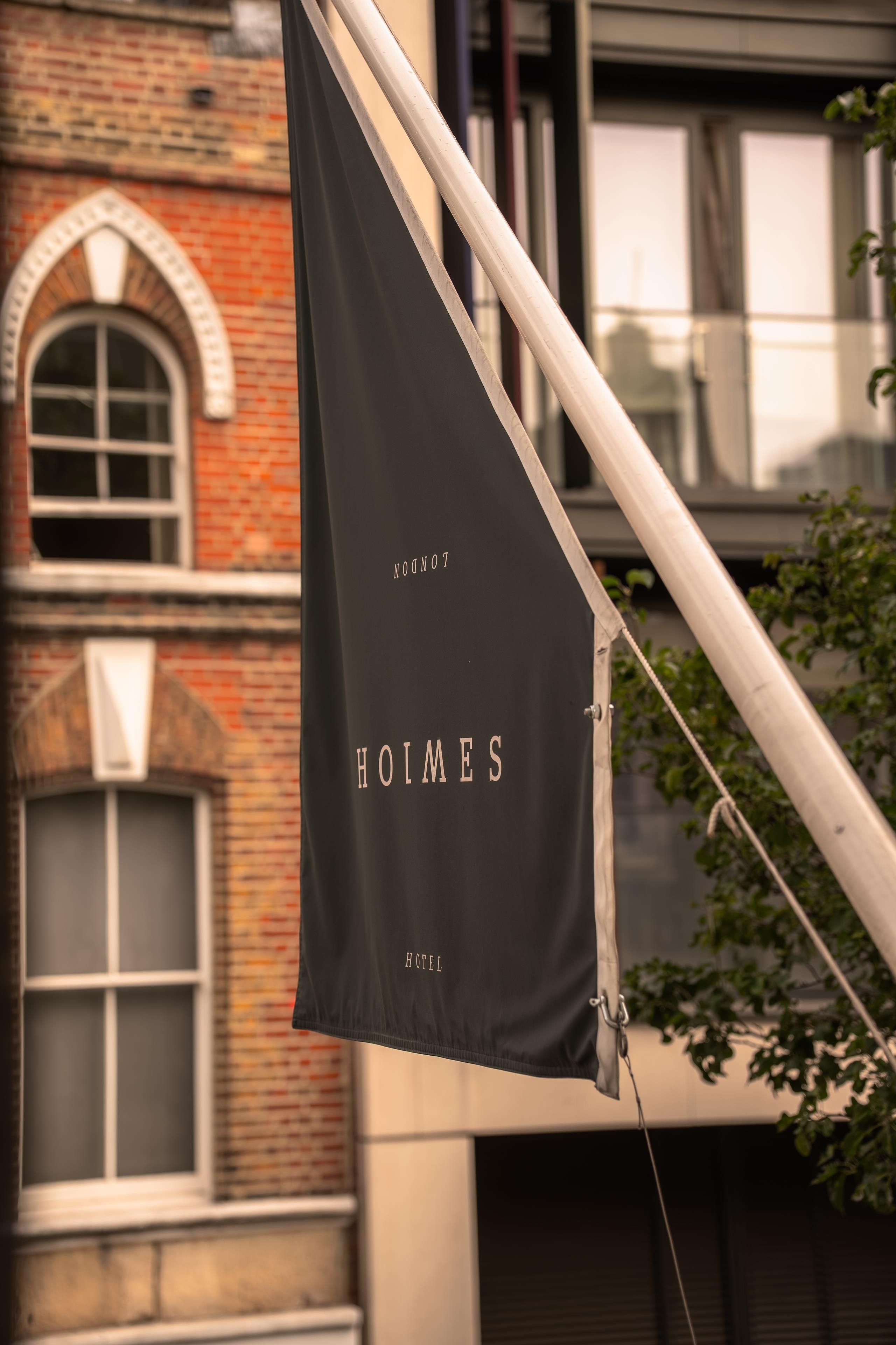 A black flag with 'HOLMES HOTEL' written on it, attached to a metal pole.