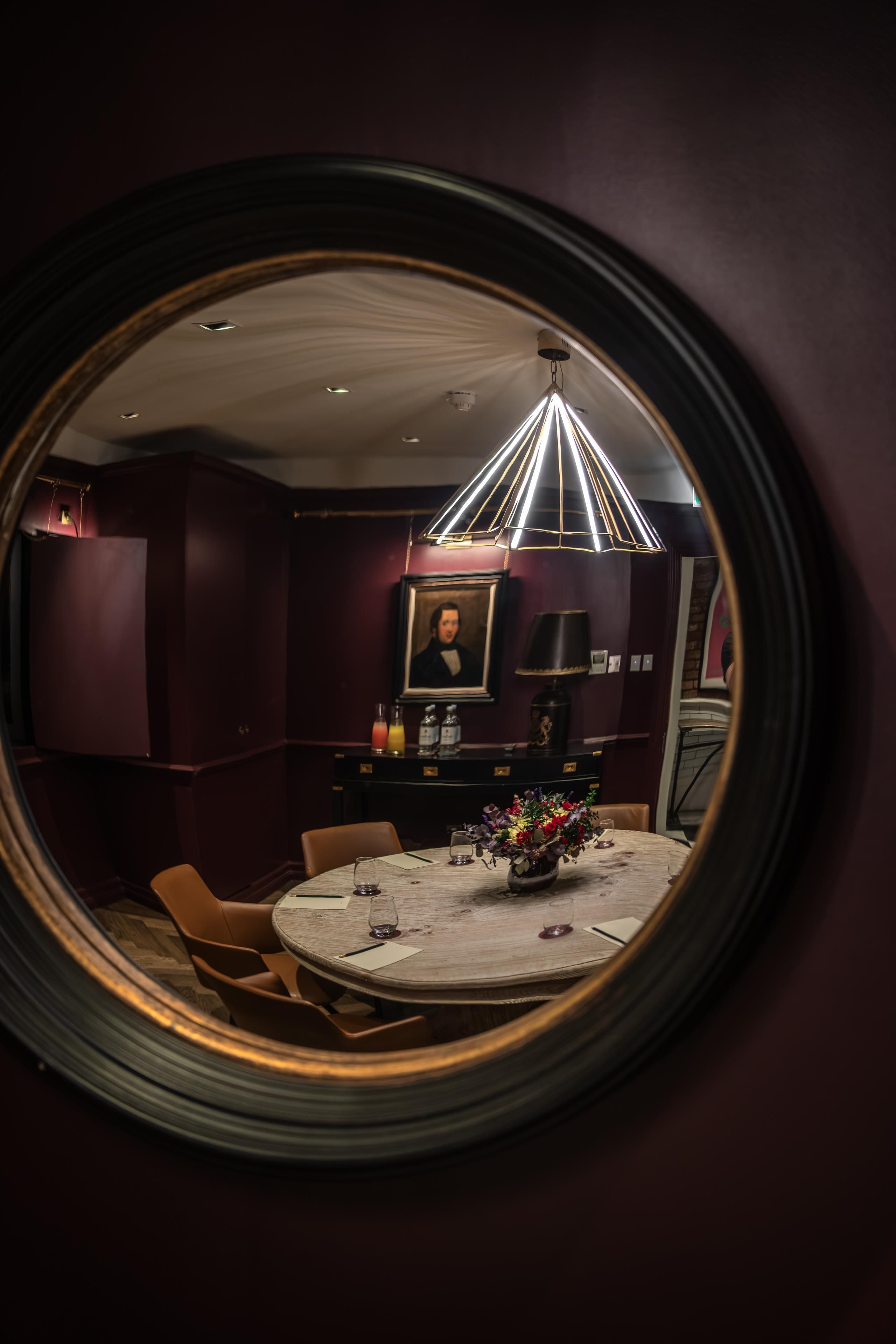 A dining area with a round table, chairs, a vase with flowers, and a ceiling light fixture.