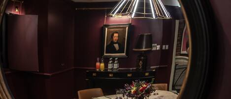 A dining area with a round table, chairs, a vase with flowers, and a ceiling light fixture.