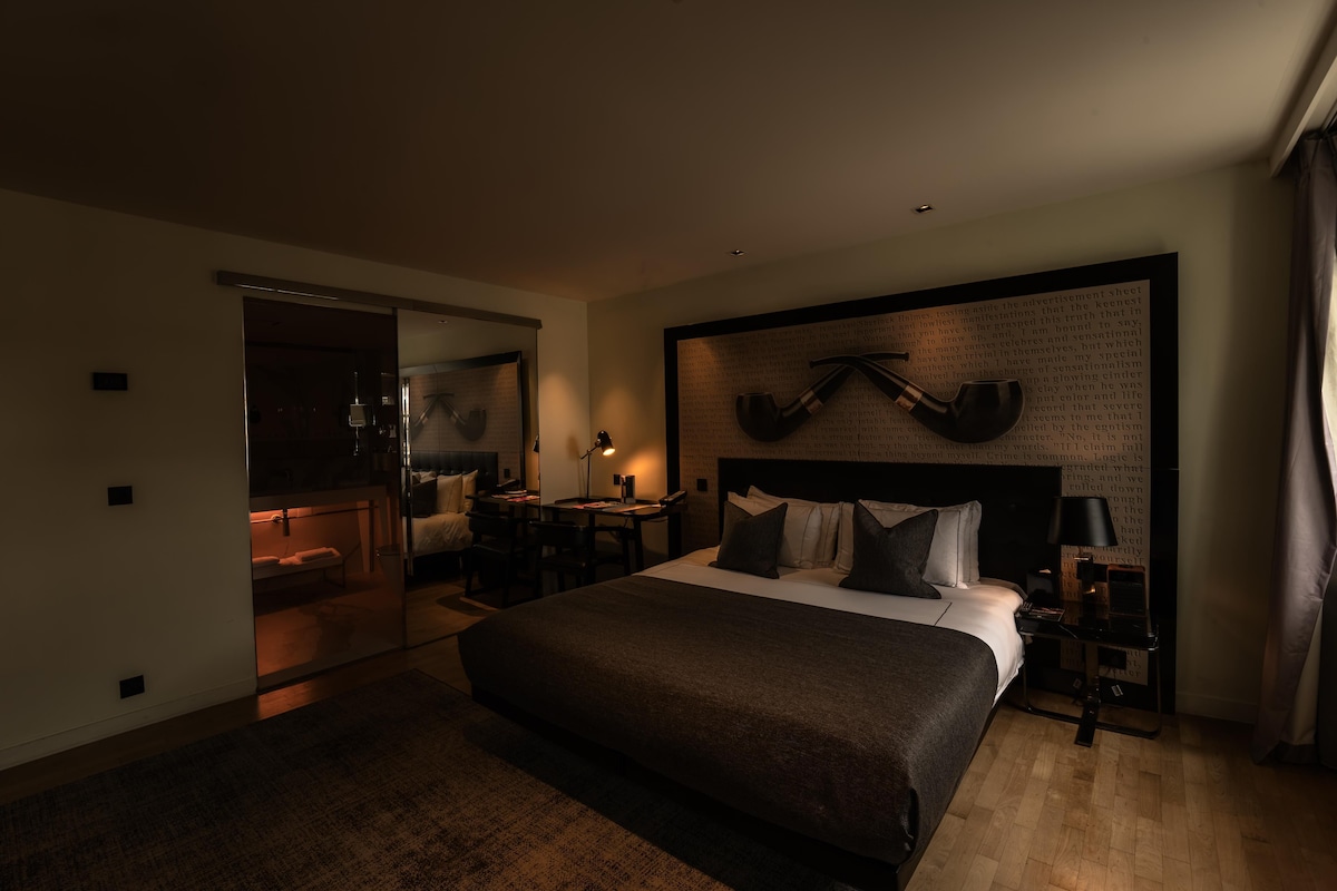 A modern hotel room with a large bed, a desk, and a mirror.