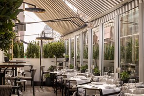 An outdoor dining area with tables and chairs, potted plants, and a striped awning. - Holmes Hotel London (London)