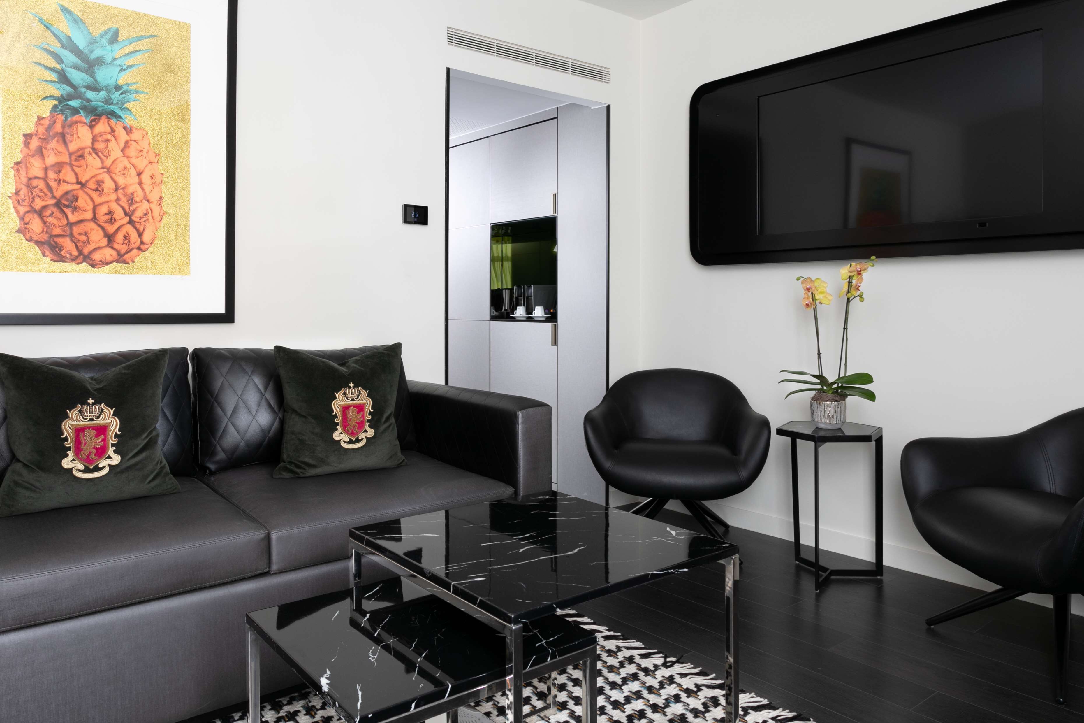 A modern living room with a sofa, two armchairs, a coffee table, and a flat-screen TV mounted on the wall.