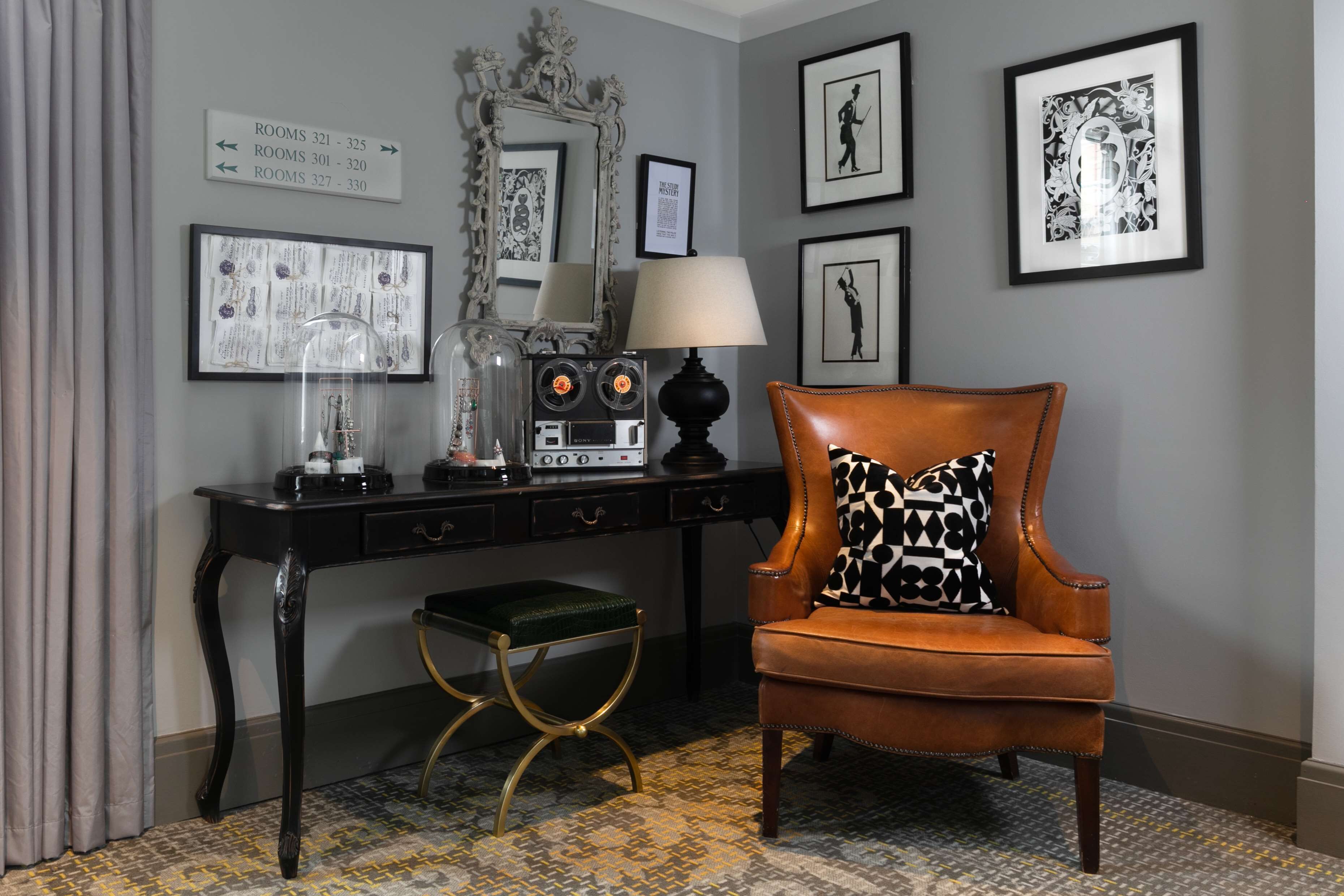 A room with a desk, a chair, a mirror, framed pictures, and a sign indicating room numbers.