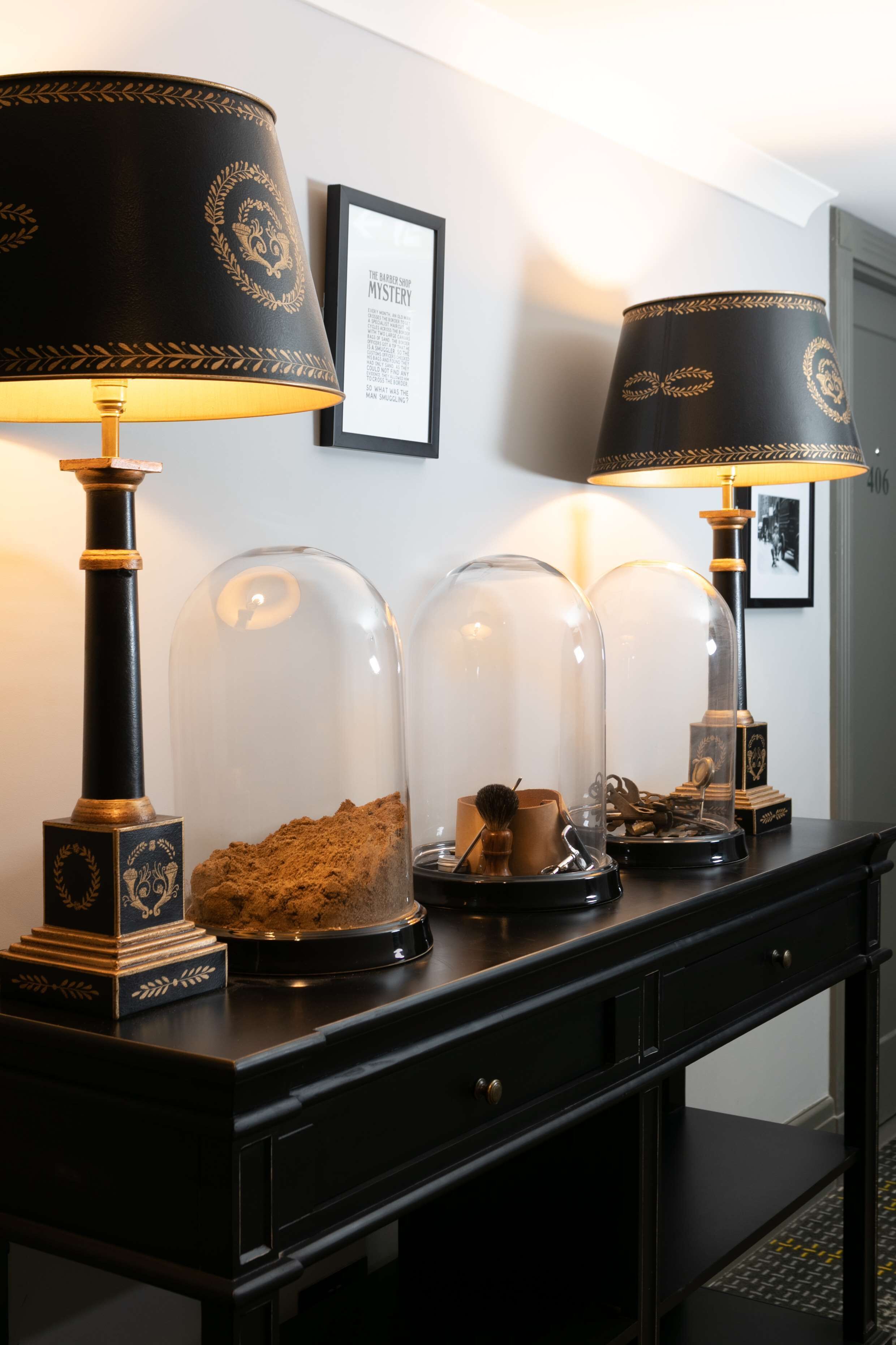 A dark wooden console table with three lamps and two glass domes containing decorative items.