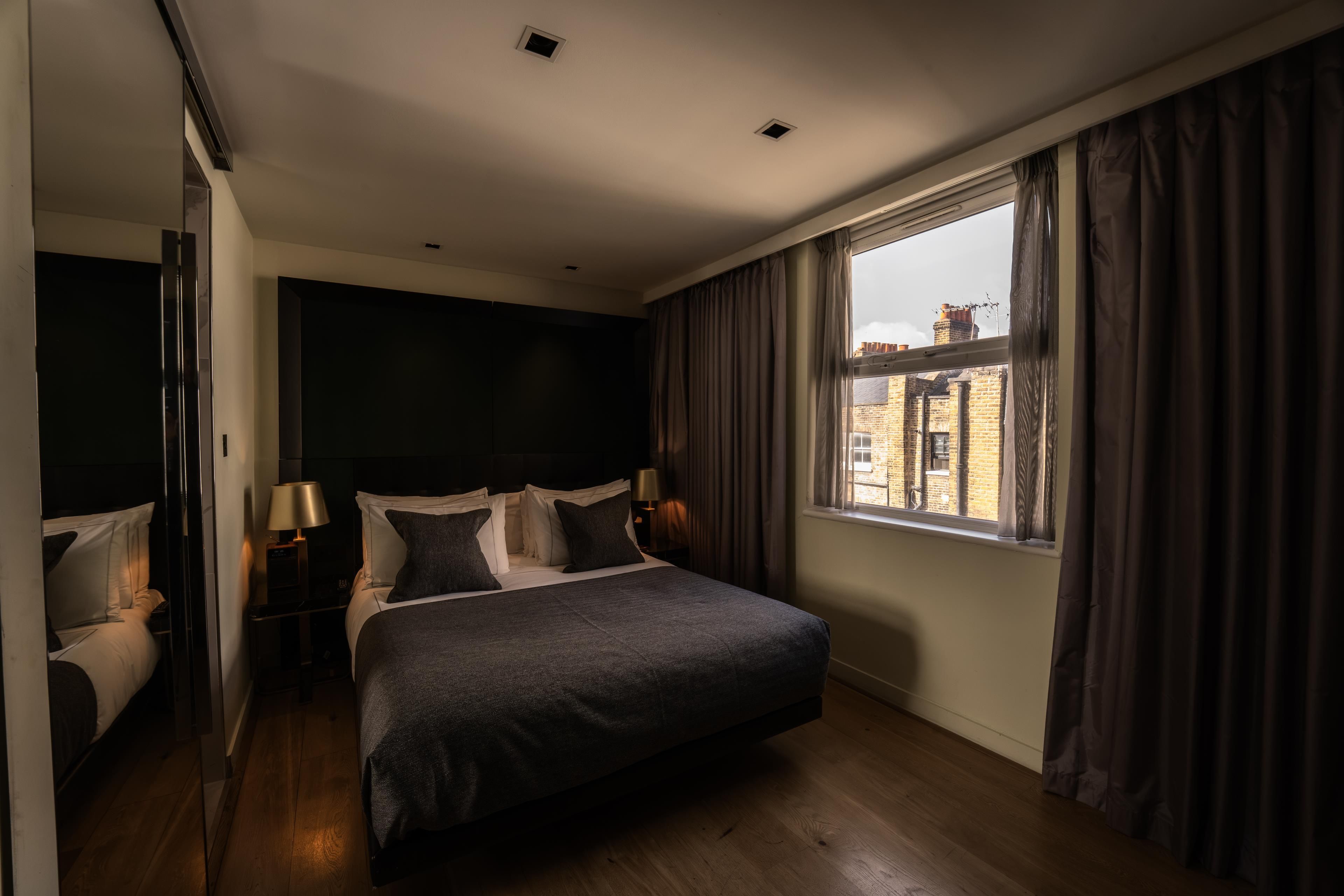 Une chambre à coucher avec un grand lit, une fenêtre avec des rideaux, une table de chevet avec une lampe et un miroir.