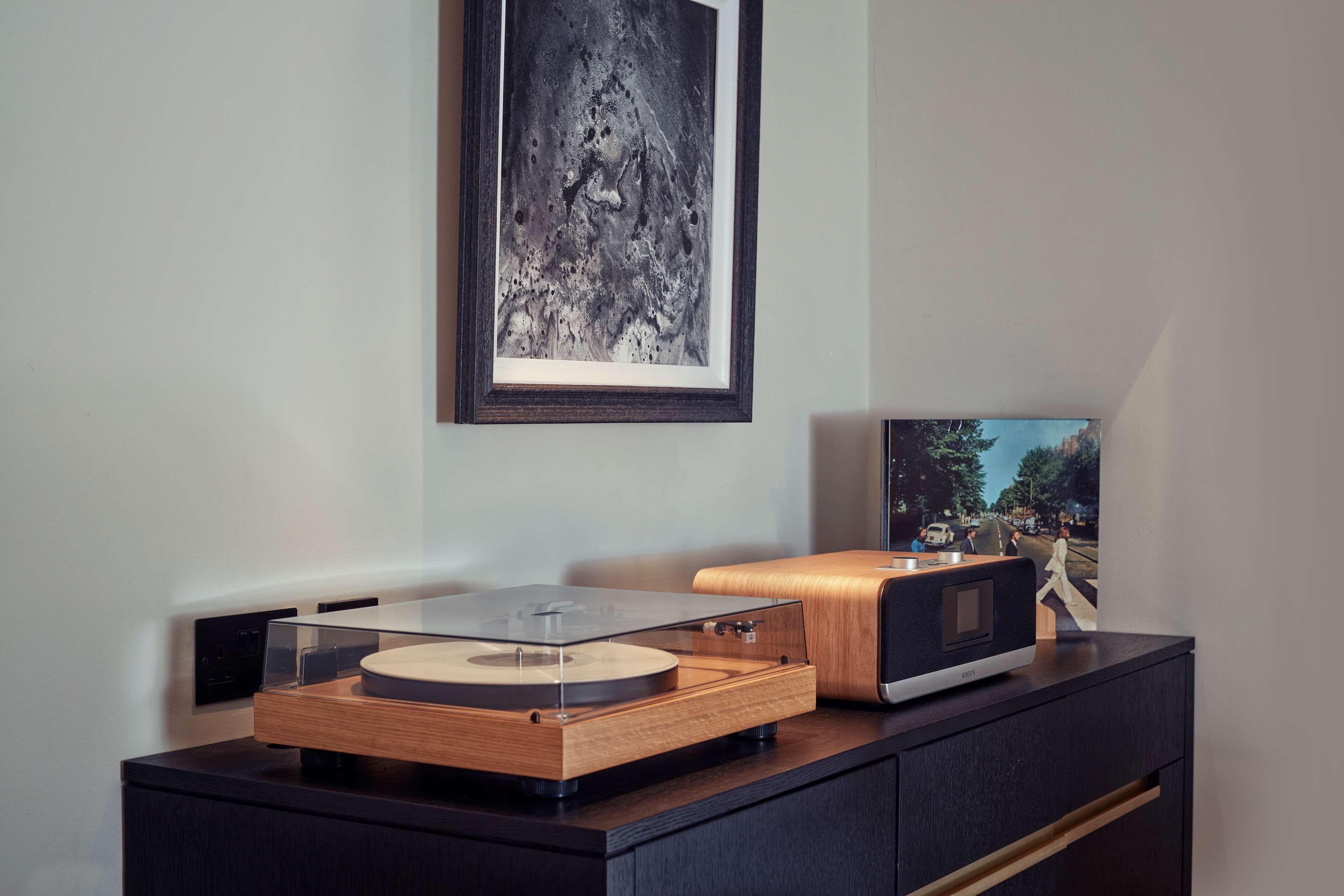 Une pièce moderne avec un meuble en bois, une platine vinyle et des œuvres d’art encadrées accrochées au mur.