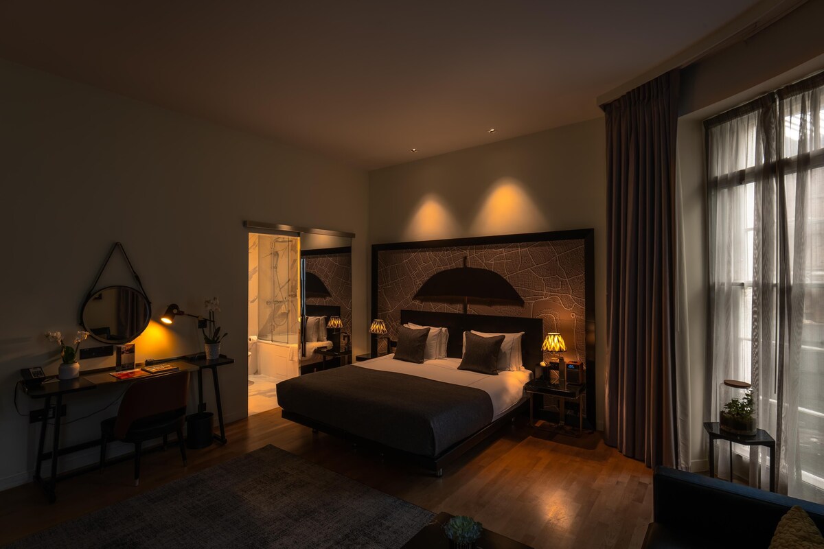 A modern hotel room with a large bed, a desk, and a sitting area.