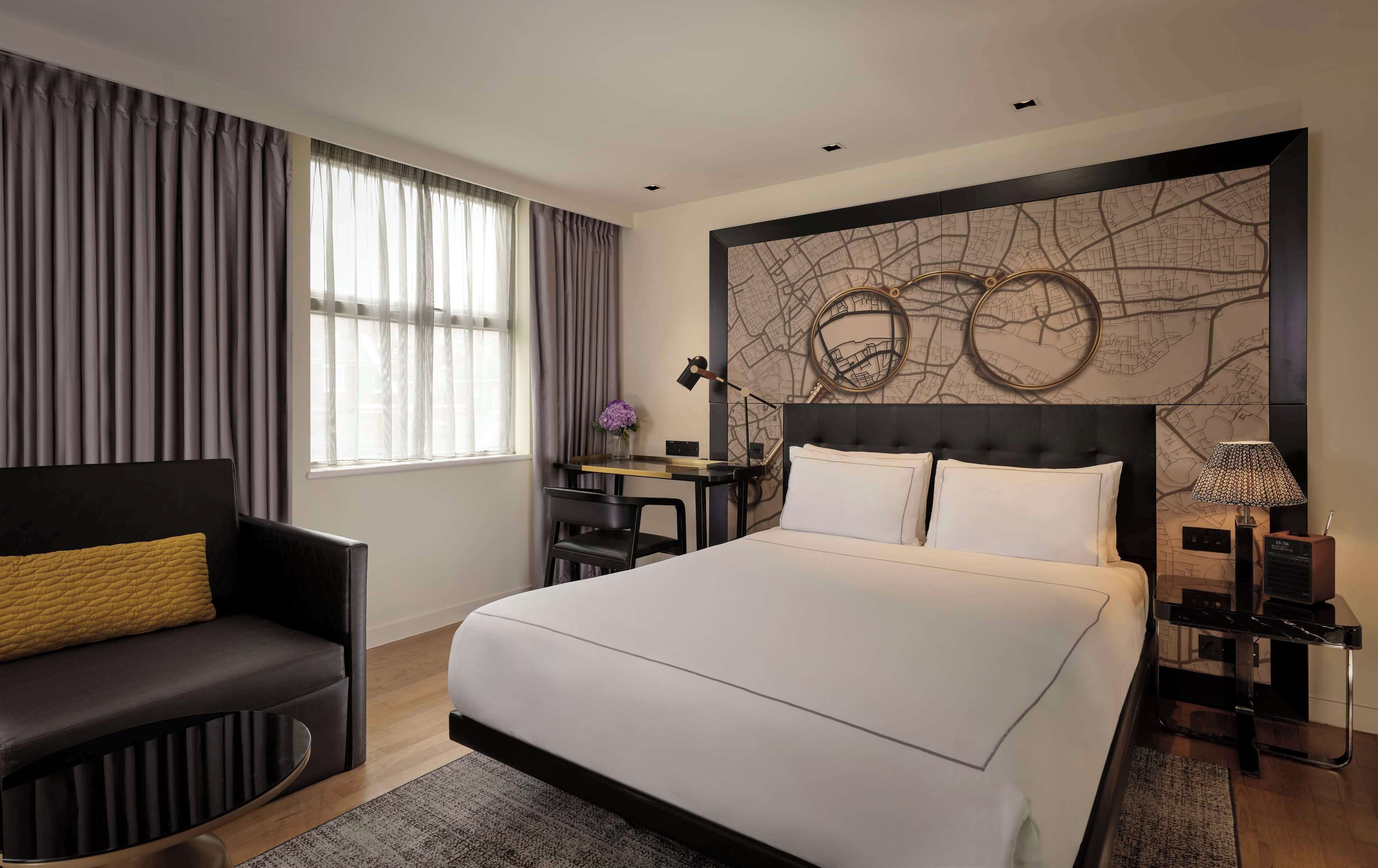 Una habitación de hotel moderna con una cama grande, un escritorio, una silla y una obra de arte con un mapa en la pared.