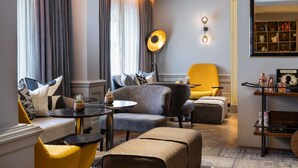 A modern living room with a sofa, armchairs, a coffee table, and a yellow armchair. There is a floor lamp, a bookshelf, and a mirror on the wall. - Holmes Hotel London (London)