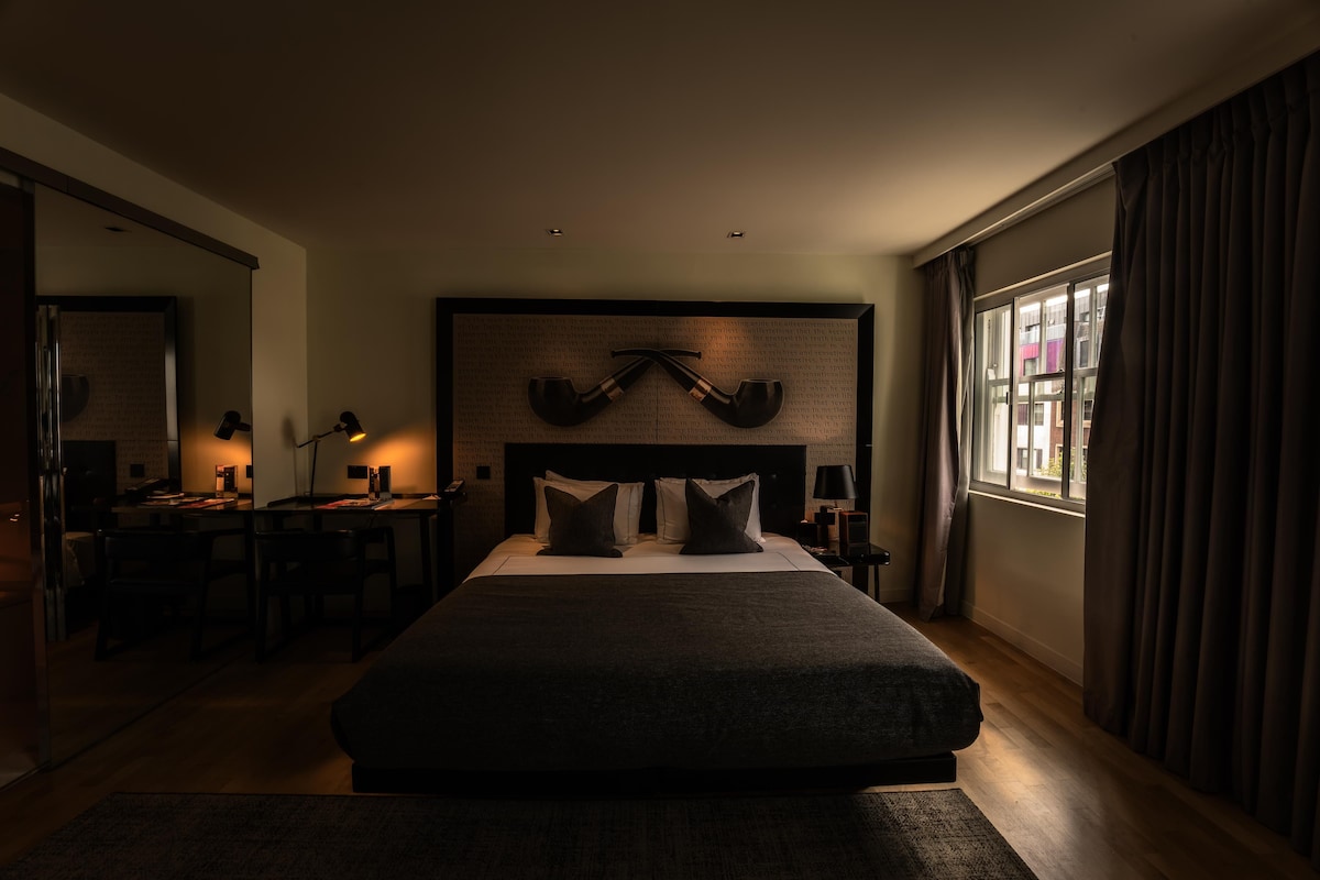 A hotel room with a large bed, bedside tables, a desk, and a window with curtains.