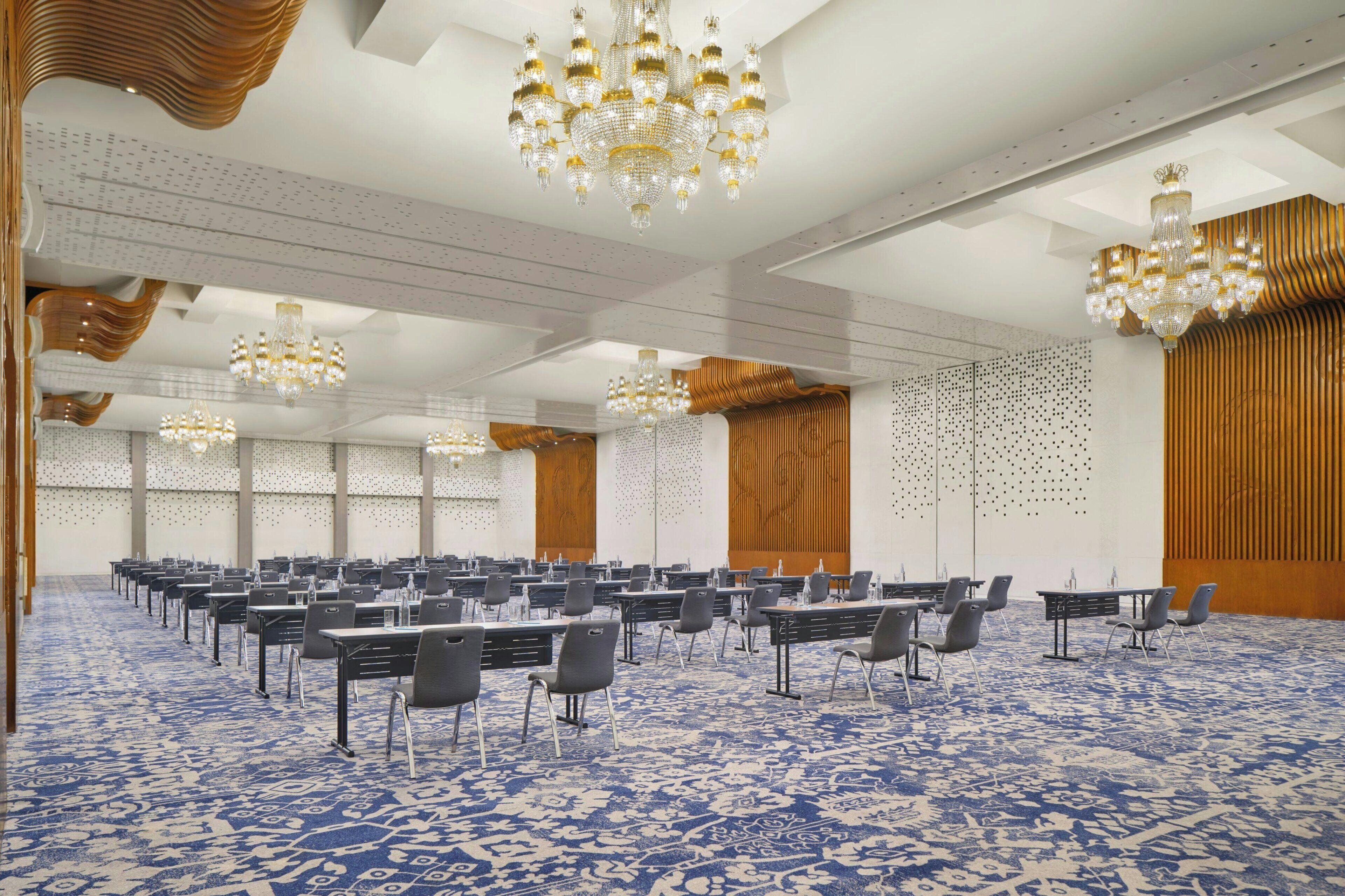 A conference room with multiple tables and chairs, large chandeliers, and a patterned carpet.