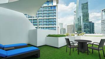 A rooftop terrace with a view of modern skyscrapers, a round table with chairs, and blue cushioned lounge areas.