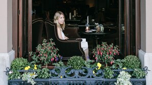 A woman sitting by a window with a decorative awning, surrounded by potted plants and a bench. - Wedgewood Hotel & Spa (Vancouver)