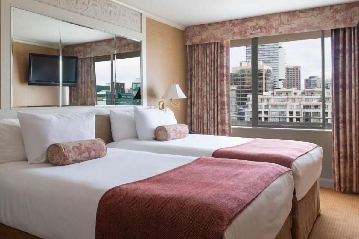 A hotel room with two beds, a TV, a phone, and a city view.