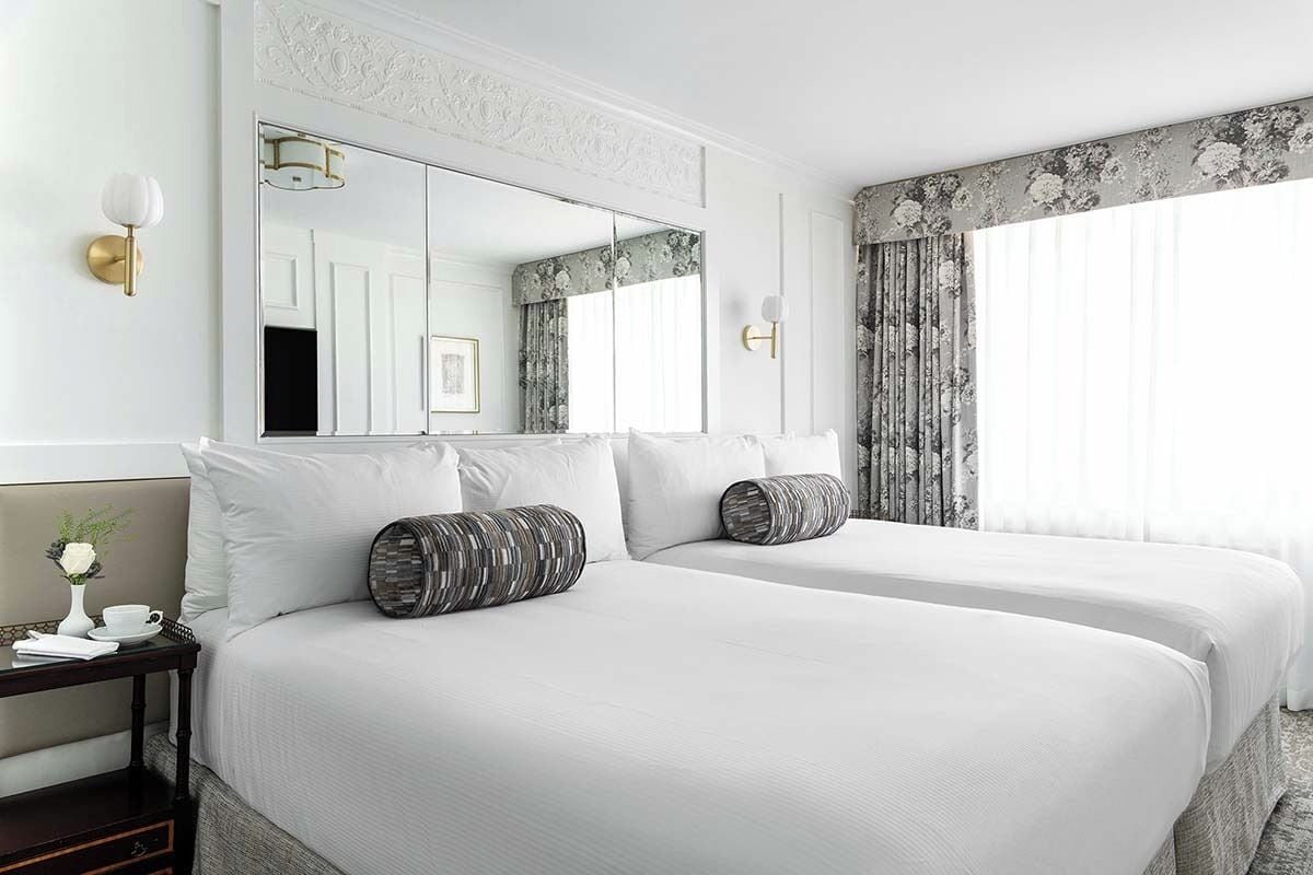 A hotel room with two beds, a large mirror, and a view of the outdoors.