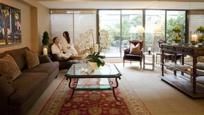 A living room with a sofa, coffee table, and chairs. There is a large window with blinds, a potted plant, and a lamp. - Wedgewood Hotel & Spa (Vancouver)