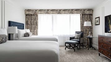 A hotel room with a large bed, a desk, a chair, a dresser, and a window with curtains.