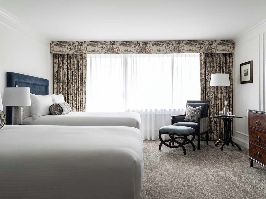 A hotel room with a large bed, a desk, a chair, a dresser, and a window with curtains.