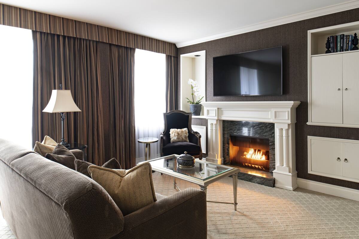 Una sala de estar con sofá, sillón, chimenea, televisión y estantería.