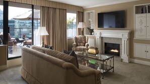 A living room with a sofa, armchairs, a fireplace, a television, and a view of the city through large windows. - Wedgewood Hotel & Spa (Vancouver)