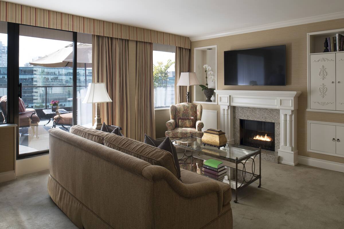 Una sala de estar con sofá, sillones, chimenea, televisor y vista a la ciudad a través de amplias ventanas.
