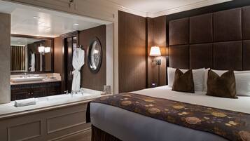 A hotel room with a large bed, a nightstand, a mirror, a bathroom with a sink and vanity, and a wall clock.