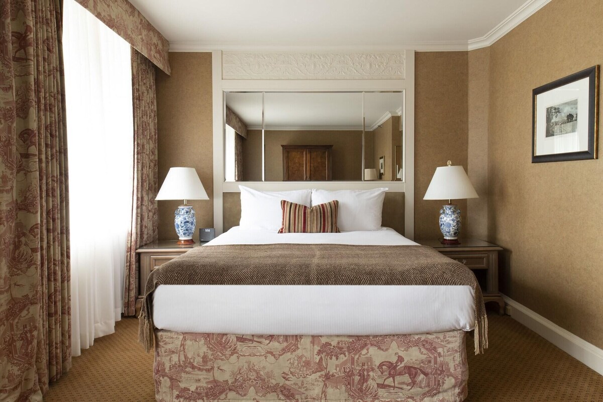 A hotel room with a large bed, two bedside tables with lamps, a mirror above the bed, and a framed picture on the wall.