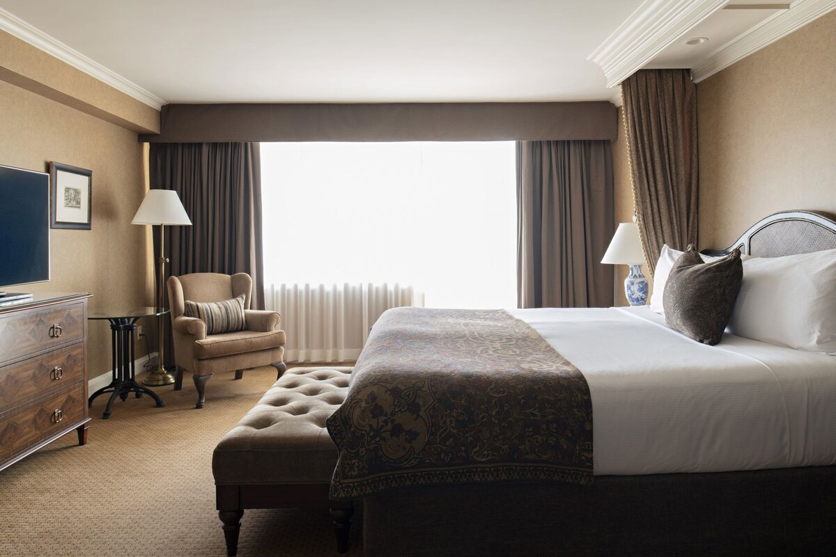 A hotel room with a large bed, a chair, a dresser, and a window with curtains.