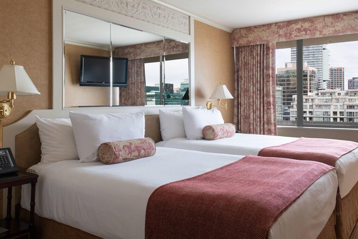 A hotel room with two beds, a TV, a phone, and a city view.