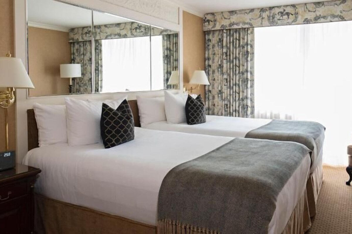A hotel room with two beds, a chair, a nightstand, and a mirror.
