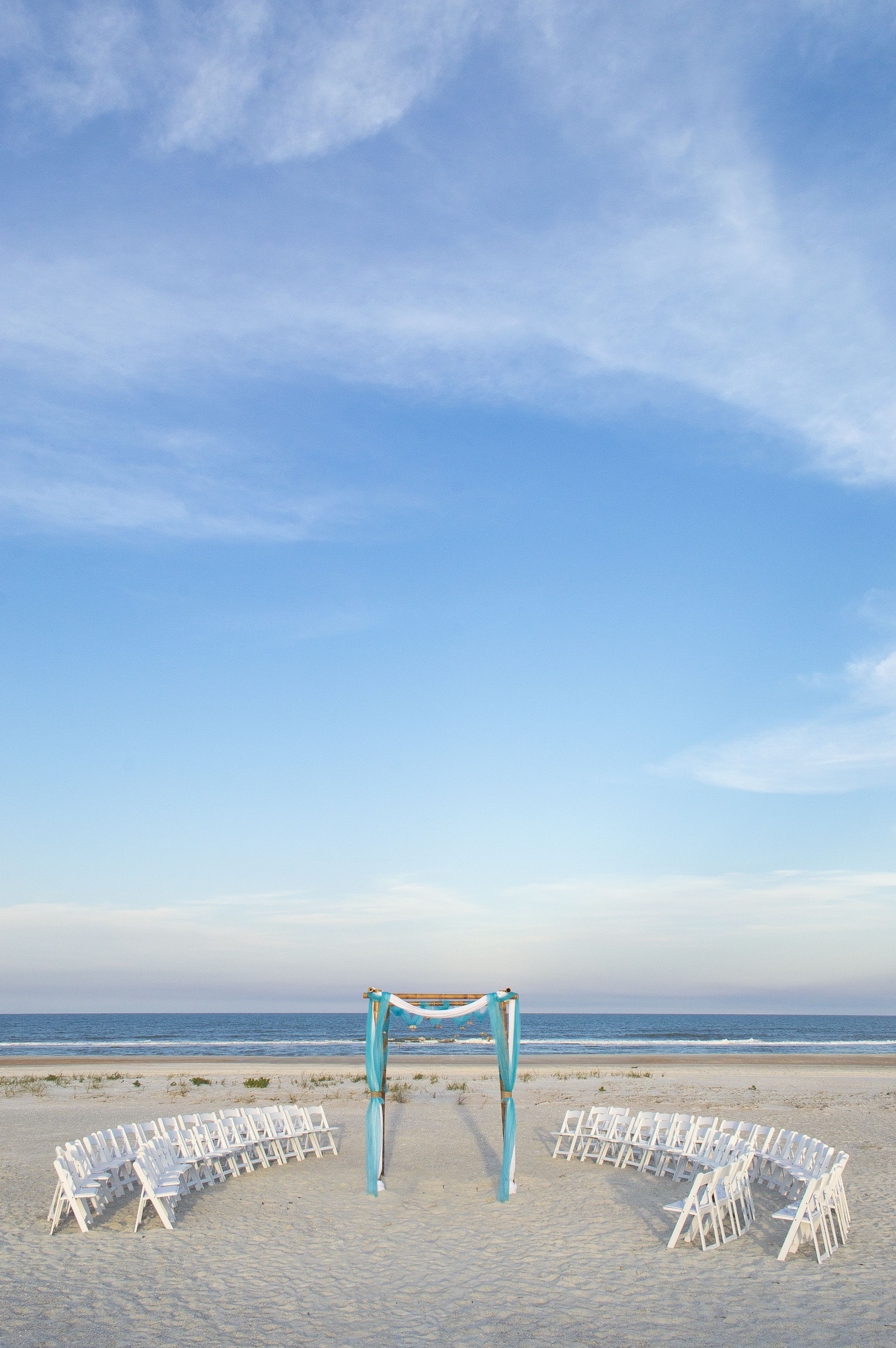 A beach ceremony setup with white chairs and a blue arch.