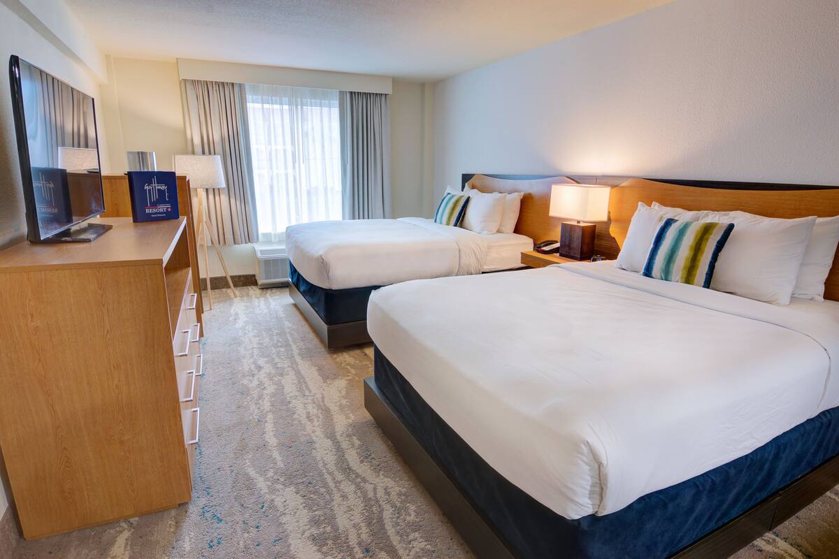 Een hotelkamer met twee bedden, een bureau met een computer, een televisie en een raam met gordijnen.