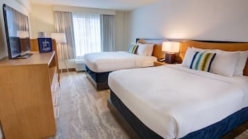 A hotel room with two beds, a desk with a computer, a TV, and a window with curtains.
