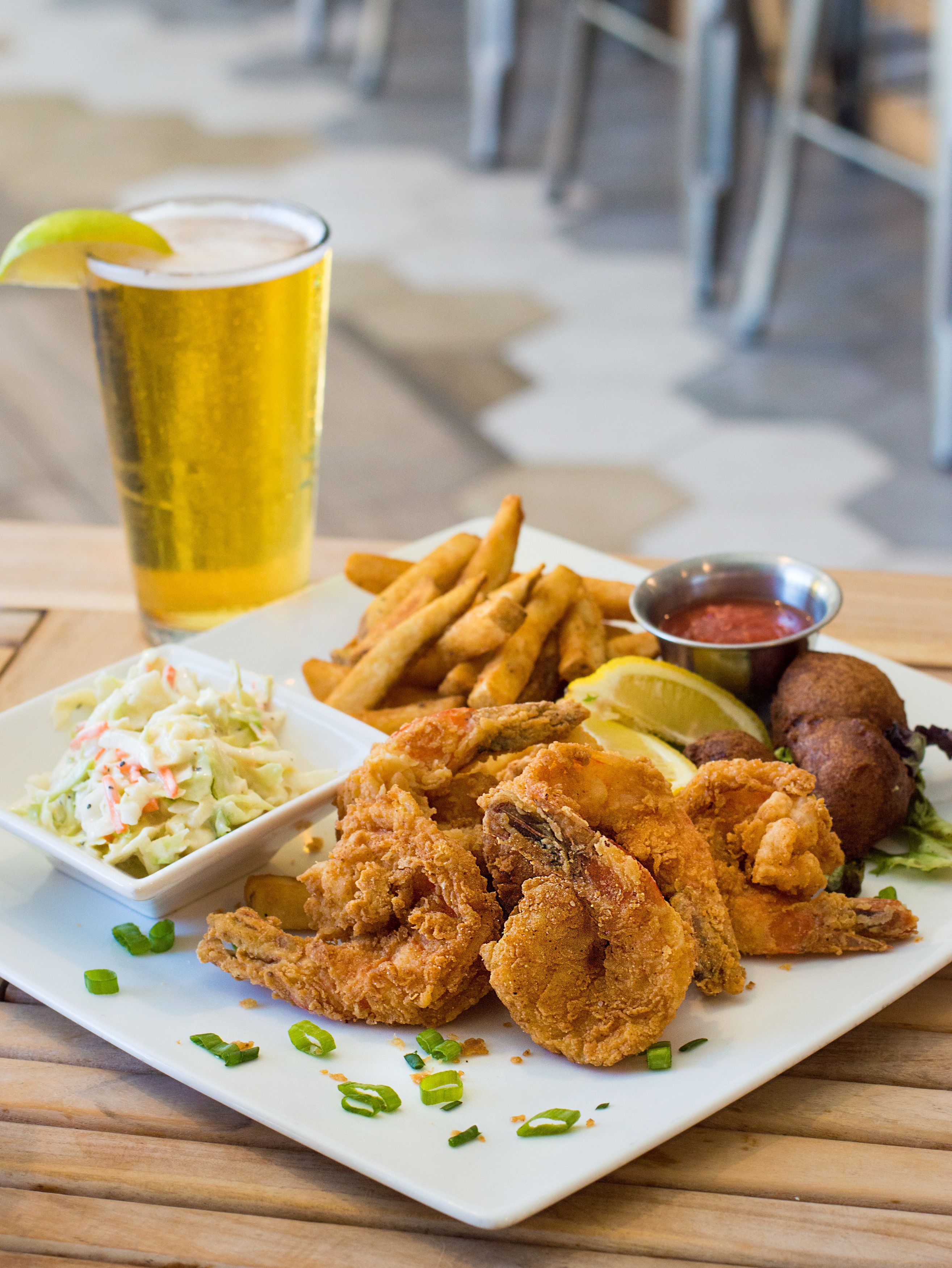 A plate of fried shrimp, fries, coleslaw, and a drink with a lemon wedge.