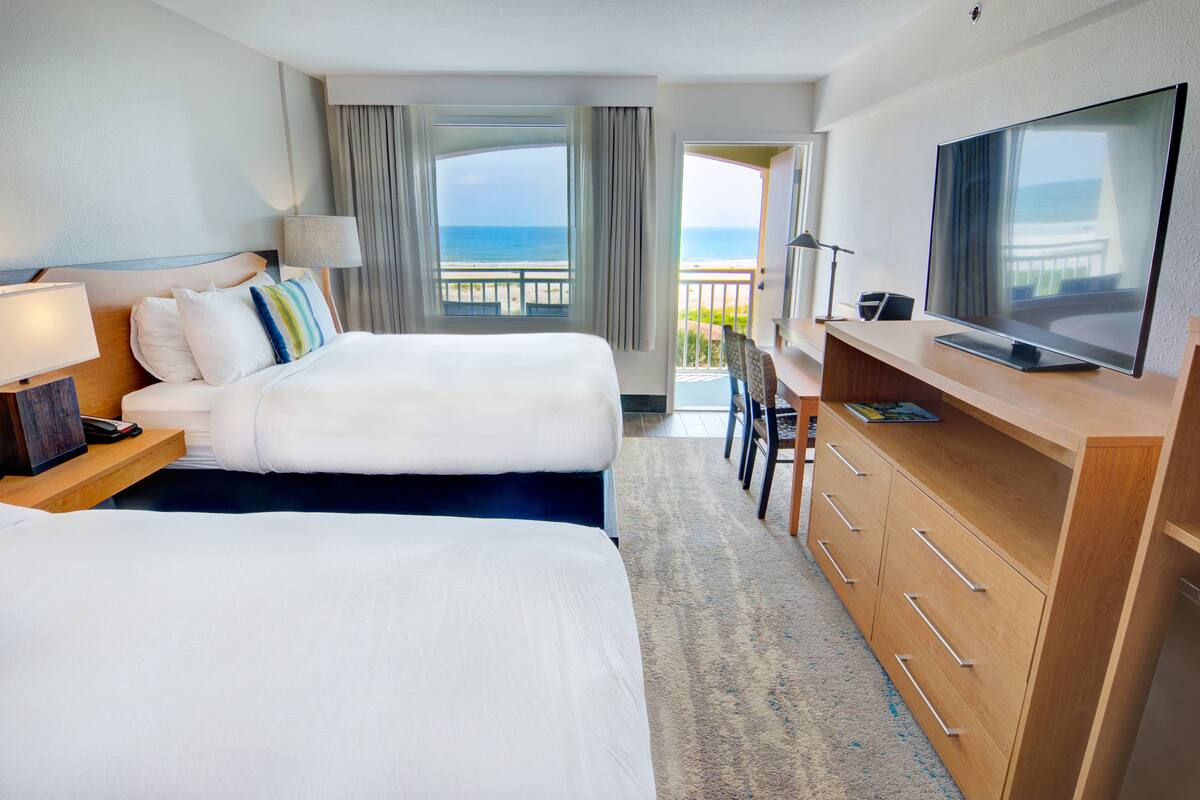 Een hotelkamer met twee bedden, een televisie, een bureau en een balkon met uitzicht op zee.