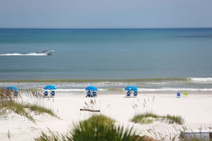 A beach with white sand, blue umbrellas, and a boat in the water. - Guy Harvey Resort on St Augustine Beach (St. Augustine)