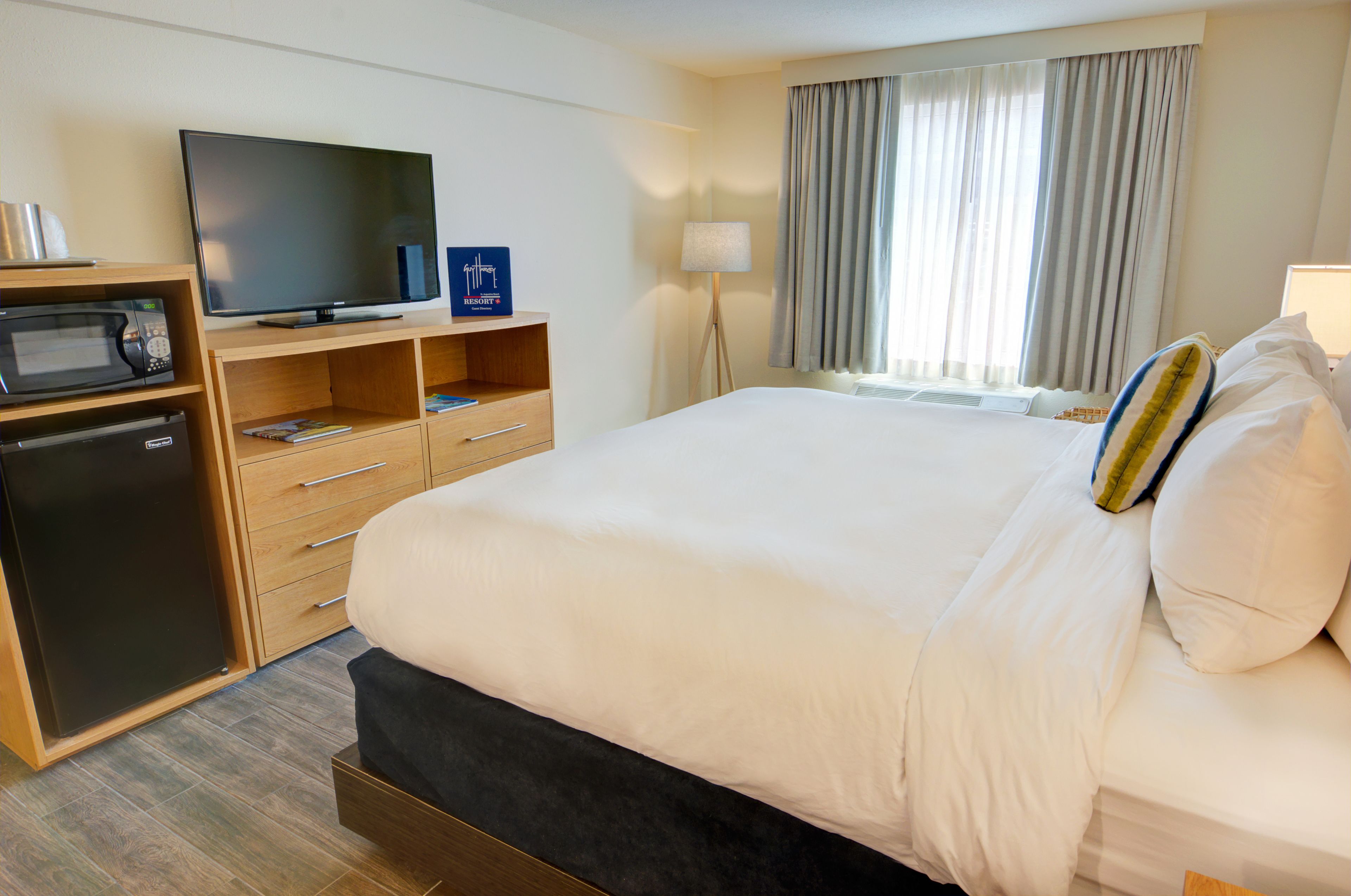 Una habitación de hotel con una cama grande, televisión, microondas y un escritorio pequeño.