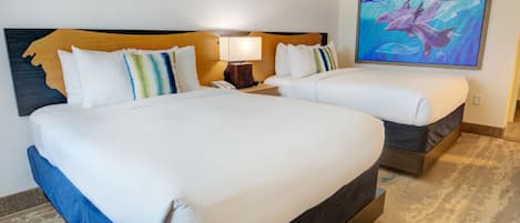 A hotel room with two beds, a wooden headboard, a nightstand with a lamp, and a painting of dolphins on the wall.