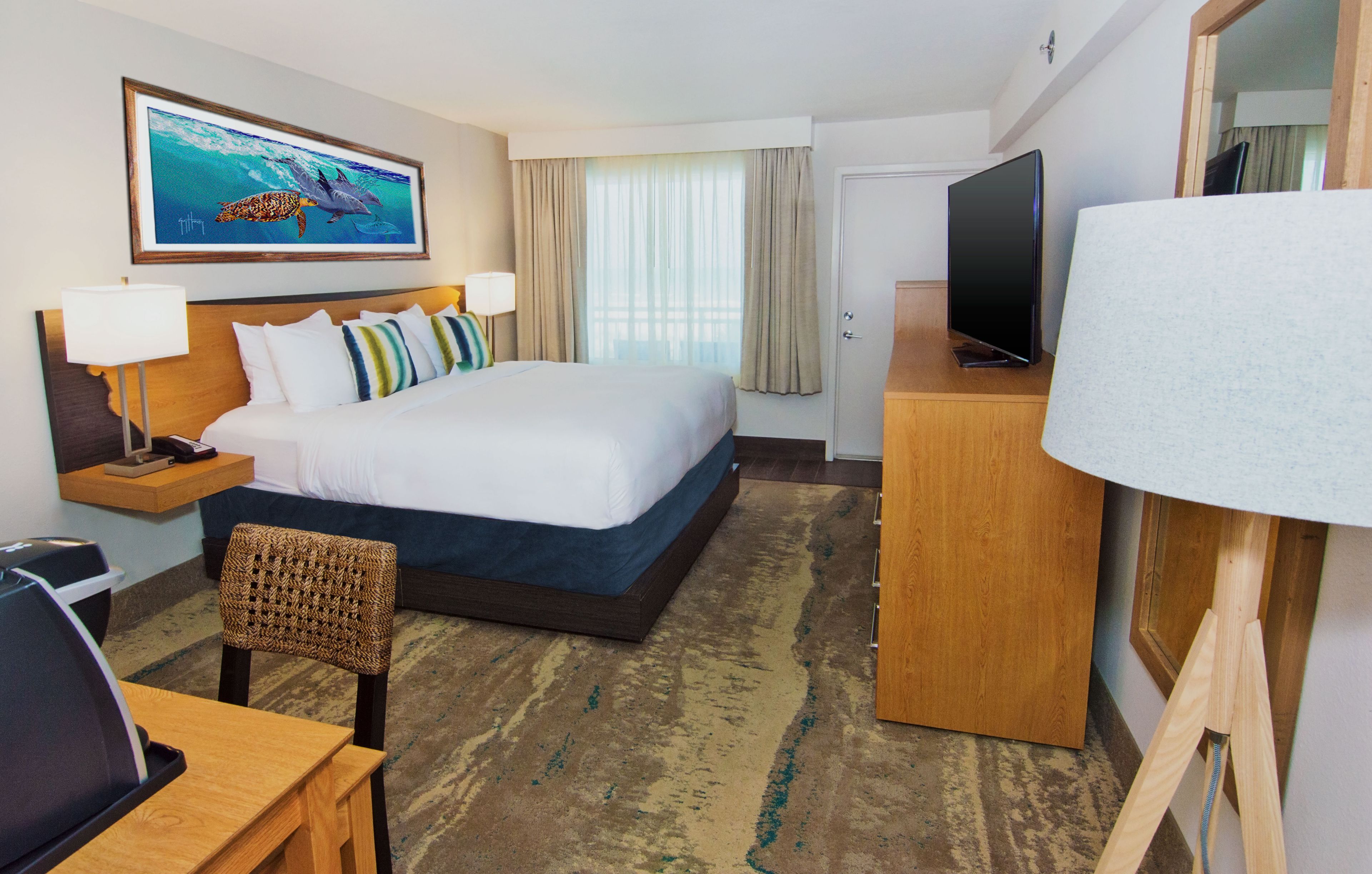 A hotel room with a large bed, a desk with a chair, a television, and a painting of dolphins on the wall.