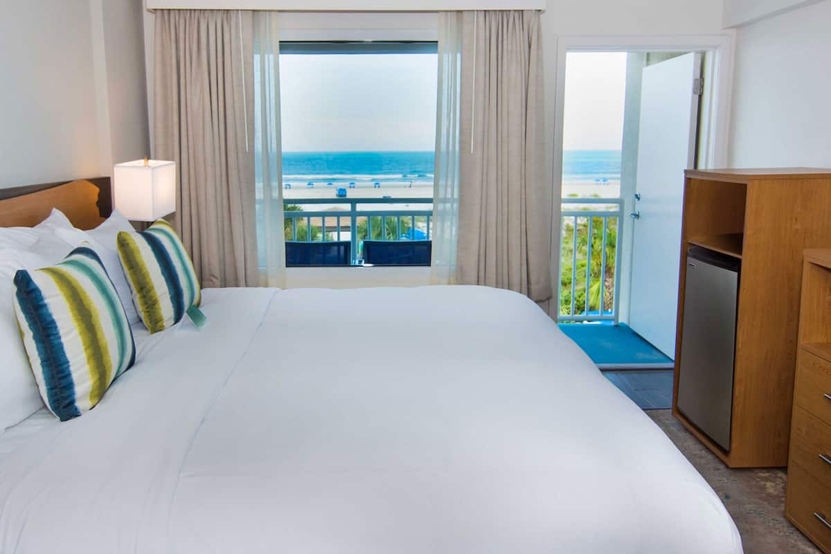 Een hotelkamer met een groot bed, uitzicht op het strand en een balkon met een hekwerk.