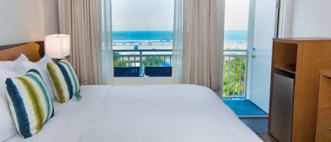 A hotel room with a large bed, a view of the beach, and a balcony with a railing.