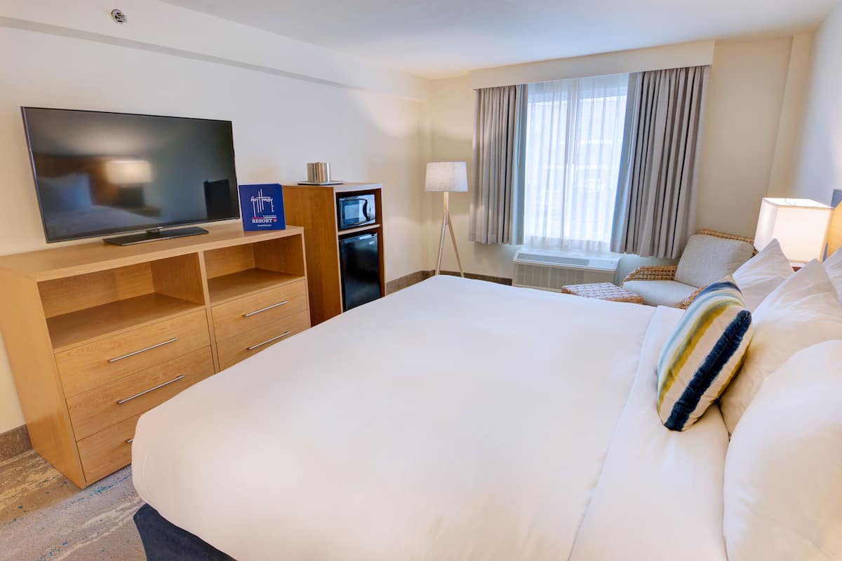 Een hotelkamer met een groot bed, een televisie, een minibar en een raam met gordijnen.