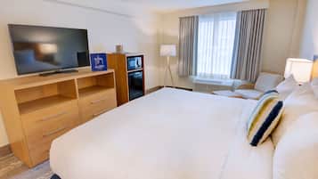Een hotelkamer met een groot bed, een televisie, een minibar en een raam met gordijnen.