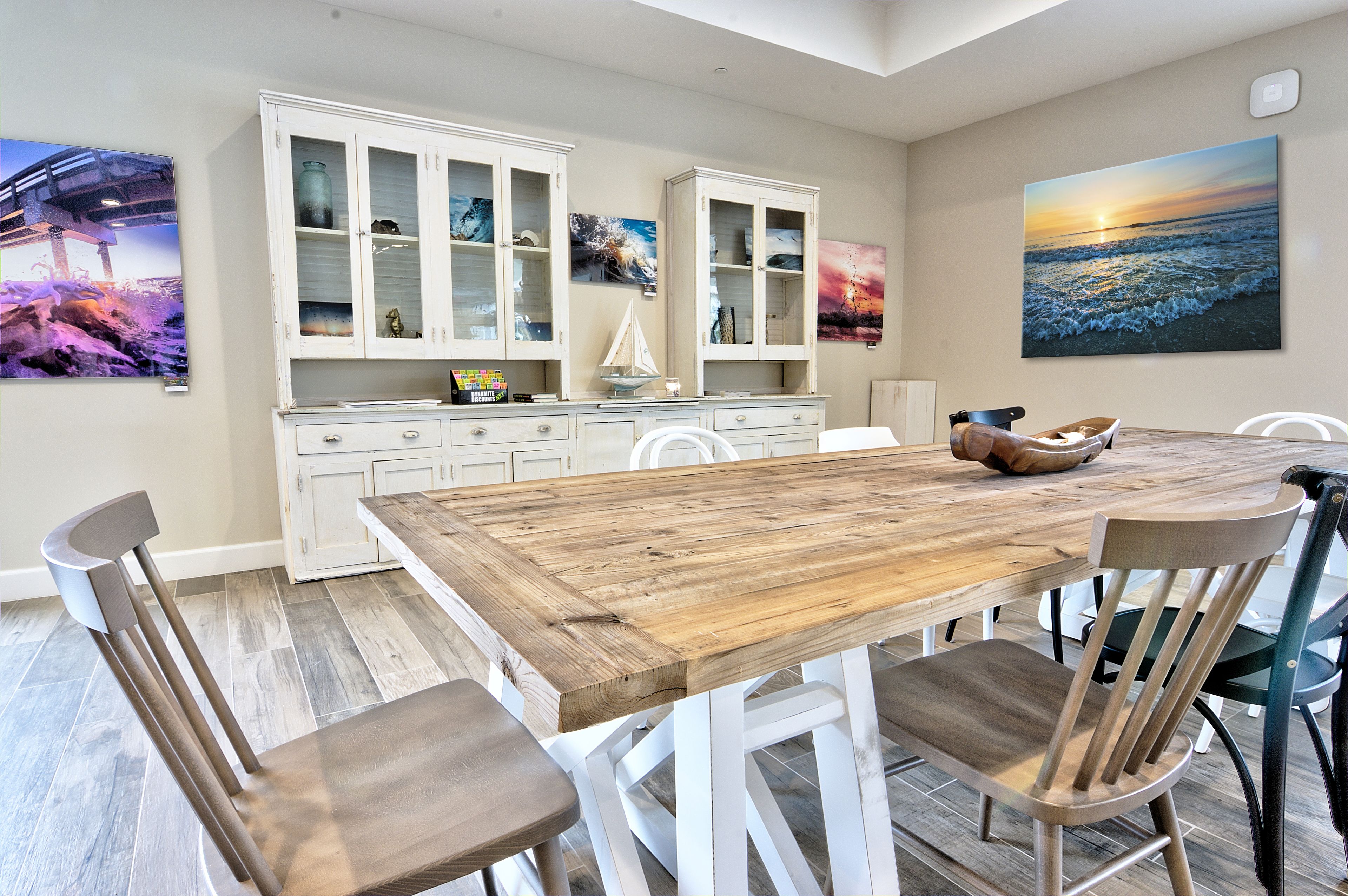 Un coin repas avec une table et des chaises en bois, des meubles blancs et des œuvres d’art accrochées aux murs.