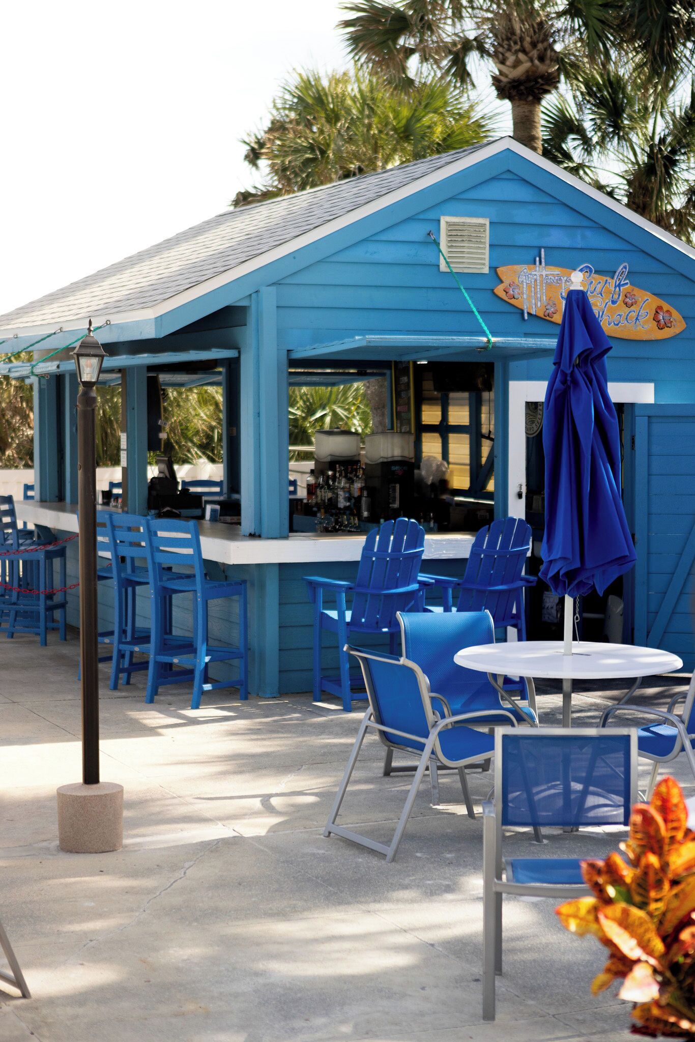 A blue outdoor seating area with chairs and tables, a bar, and a sign that reads "Surf Shack."