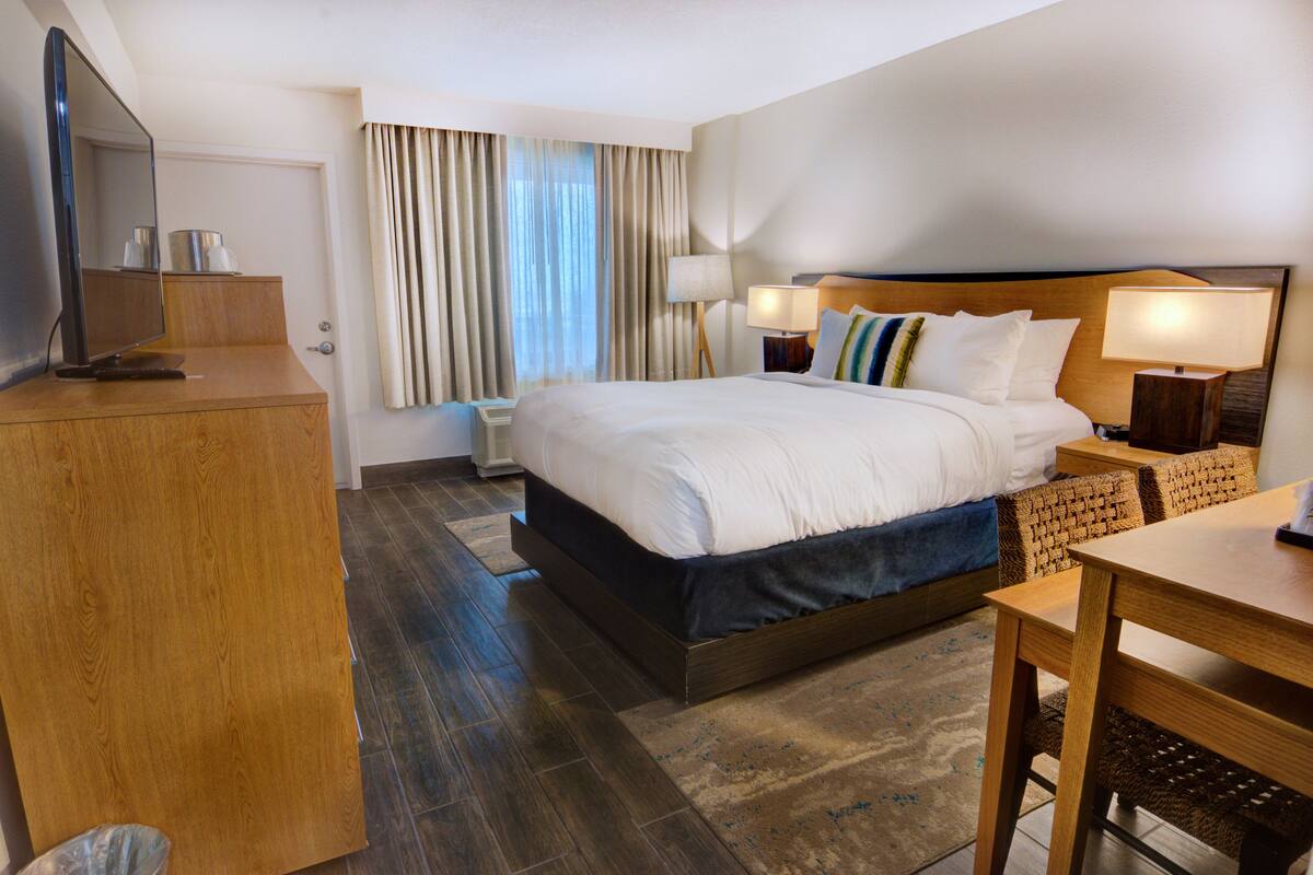 Een hotelkamer met een groot bed, nachtkastjes met lampen, een houten bureau, een televisie en een raam met gordijnen.