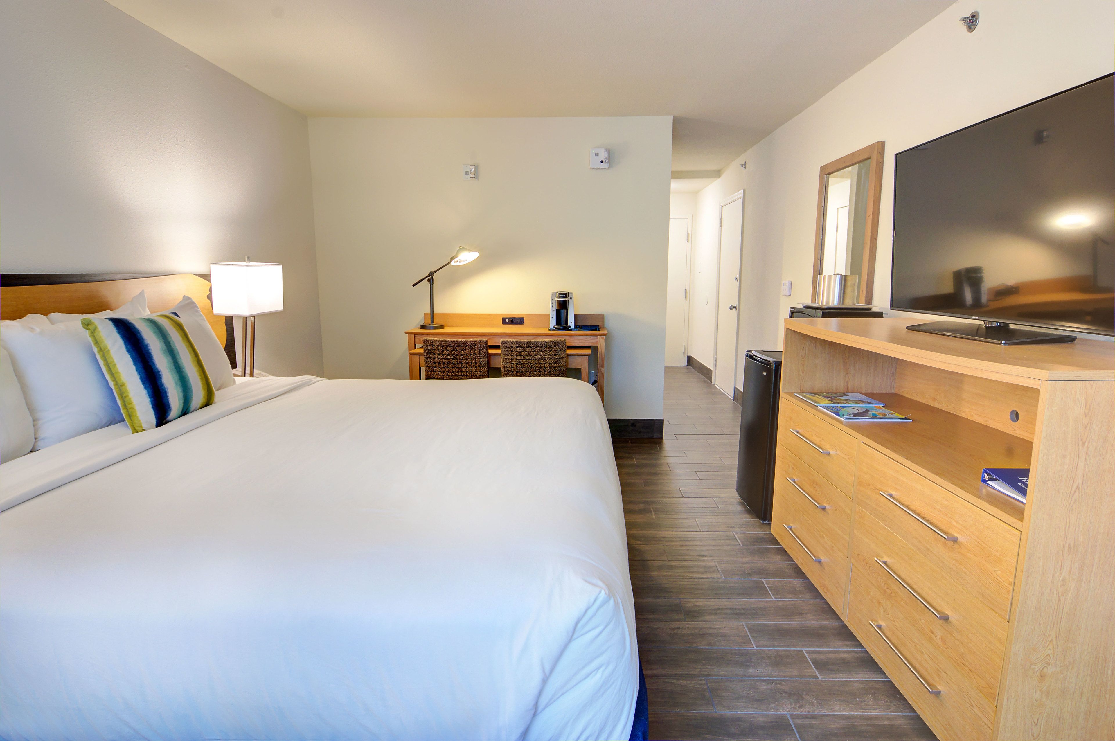 Ein Hotelzimmer mit einem großen Bett, einem Schreibtisch mit Lampe, einem Fernseher und einer Holzkommode.