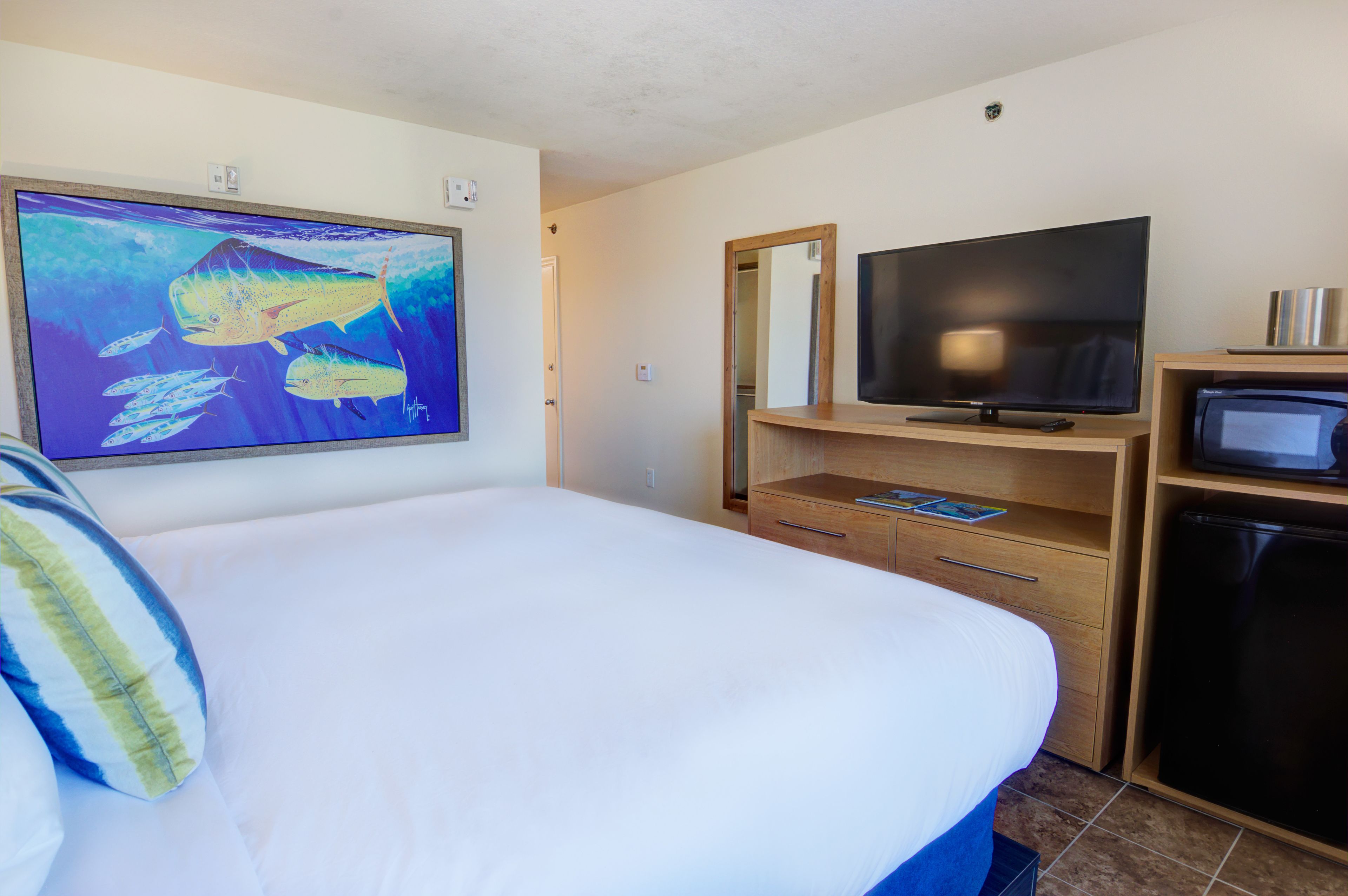Een hotelkamer met een bed, een televisie, een koelkast, een houten dressoir en een groot, ingelijst beeld van vissen aan de muur.